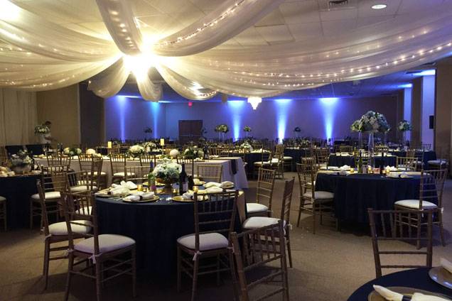 Elegant ballroom setup with navy blue tablecloths, floral centerpieces, and draped ceiling lights creating a warm, inviting atmosphere