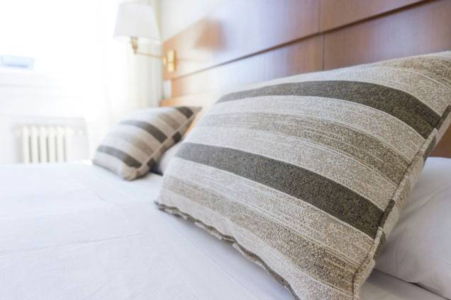 Close-up of a neatly made hotel bed with striped pillows and a wooden headboard in a bright, sunlit room.