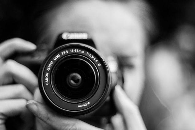 Close-up of a person holding a Canon camera, focusing through the lens to take a photo.