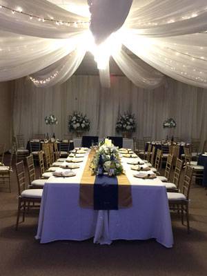 Elegant wedding reception setup in The Pavilion Ballroom with draped ceiling lights, floral arrangements, and a long banquet table.
