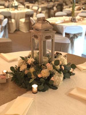 Elegant wedding table centerpiece in The Pavilion Ballroom featuring a rustic lantern, white flowers, and greenery.