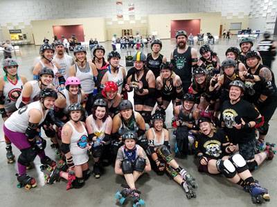 Roller derby teams posing together on the floor of The Pavilion Expo Hall after a match.