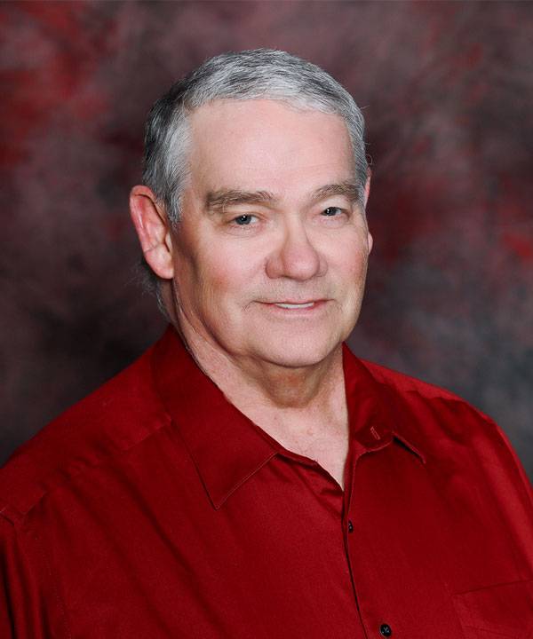 Professional headshot of The Pavilion Venue Coordinator, Charles Jarvis, wearing a red shirt against a studio backdrop.