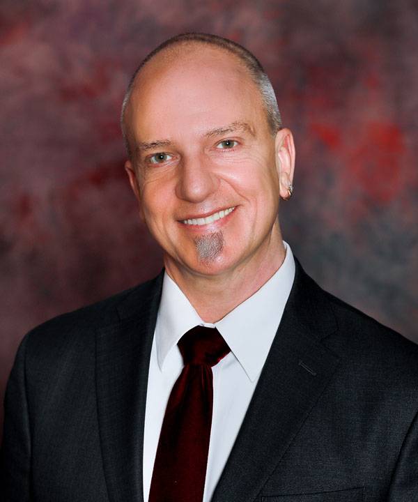 Professional headshot of The Pavilion Executive Director, Jared Garrison, wearing a dark suit with a maroon tie against a studio backdrop