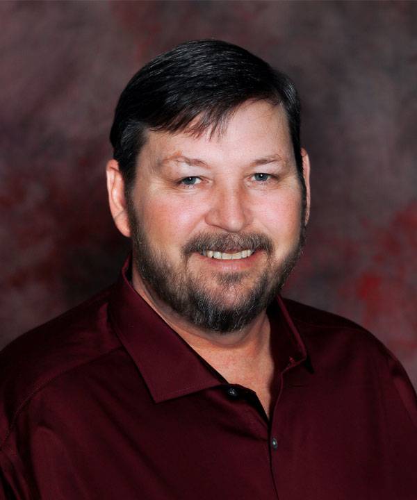 Professional headshot of The Pavilion Logistics Liaison, Kenneth Furlong, wearing a maroon shirt against a studio backdrop.