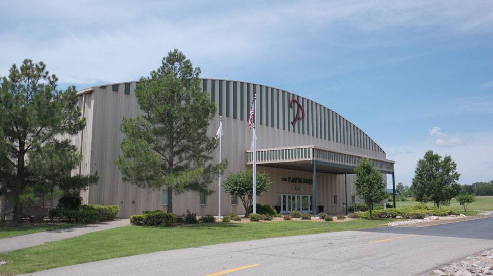 Exterior view of The Pavilion event venue with arched roof, front entrance, and surrounding trees on a sunny day.