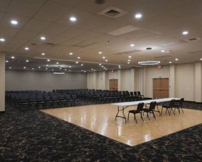 Wide view of The Pavilion Ballroom arranged for a conference with chairs, tables, and ceiling lights over a polished wood floor.