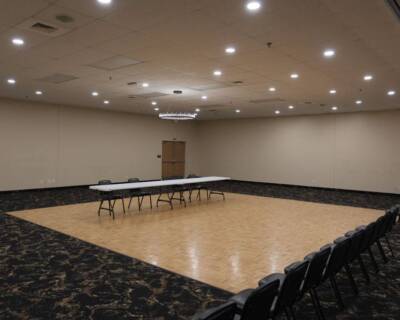 Spacious ballroom at The Pavilion with polished wood floor, conference table, and rows of chairs under ceiling lights