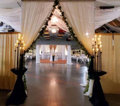 The Pavilion Expo Hall decorated for a wedding with draped fabric, chandeliers, and candlelit entrance leading to the reception area.
