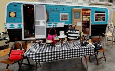 Vendor booth inside The Pavilion Expo Hall featuring a vintage turquoise camper and display table with handbags and jewelry.