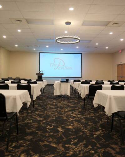 Meeting room at The Pavilion set up classroom-style with tables, chairs, podium, and presentation screen.